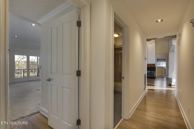 corridor with a textured ceiling, recessed lighting, wood finished floors, baseboards, and crown molding