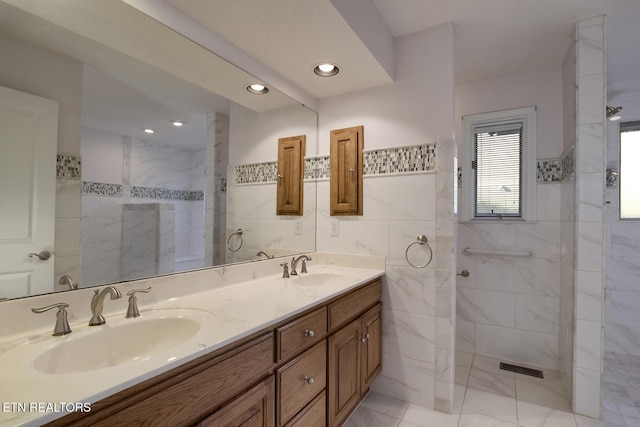 bathroom with tile walls, a walk in shower, and a sink