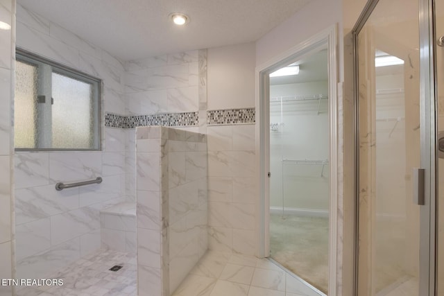 bathroom featuring marble finish floor, a tile shower, a walk in closet, and a textured ceiling