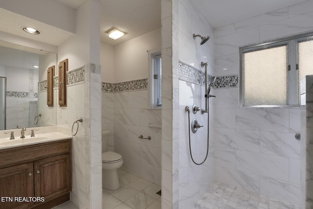 full bath with toilet, vanity, a tile shower, and tile walls