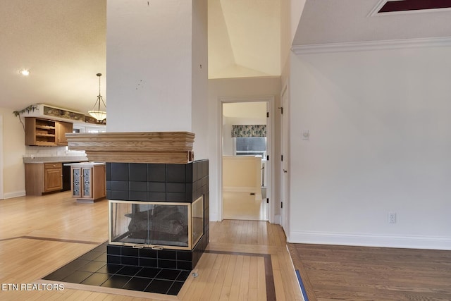 living room featuring a tile fireplace, crown molding, light wood-style flooring, and baseboards