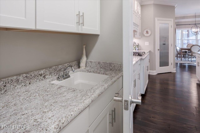 interior space with dark wood finished floors, ornamental molding, a sink, stainless steel gas stovetop, and a notable chandelier