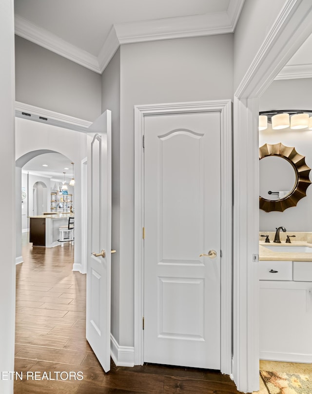 hallway featuring crown molding, arched walkways, a sink, and wood finished floors