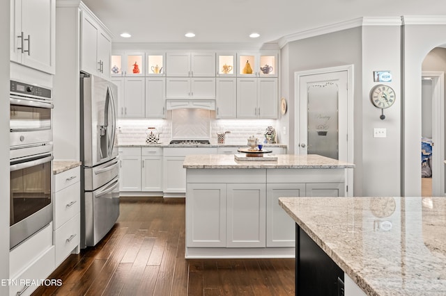 kitchen with dark wood-type flooring, white cabinets, appliances with stainless steel finishes, tasteful backsplash, and crown molding