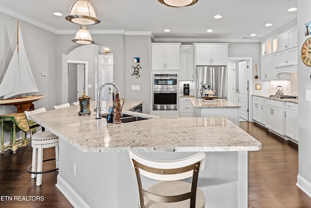 kitchen with arched walkways, a kitchen island with sink, stainless steel appliances, a sink, and decorative backsplash