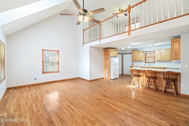 unfurnished living room with a ceiling fan, baseboards, high vaulted ceiling, and light wood finished floors