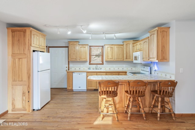 kitchen with white appliances, light brown cabinets, a sink, and a peninsula