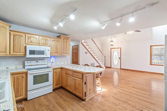 kitchen featuring white appliances, a breakfast bar area, open floor plan, a peninsula, and light wood-type flooring