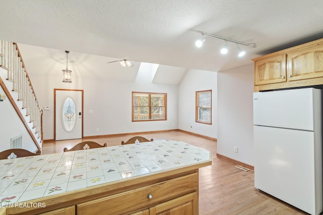 kitchen featuring light wood finished floors, visible vents, tile counters, freestanding refrigerator, and a textured ceiling