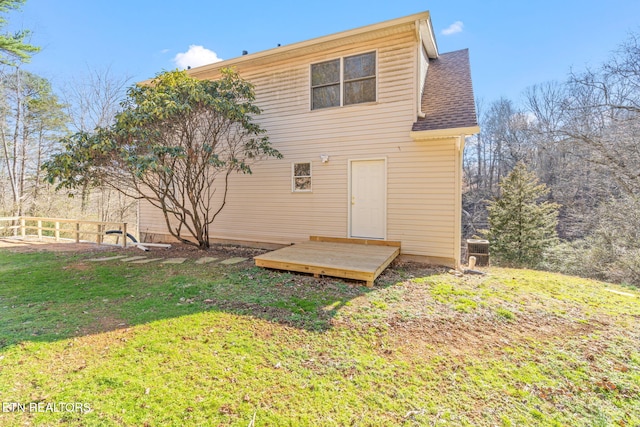 rear view of property with a shingled roof, fence, and a lawn