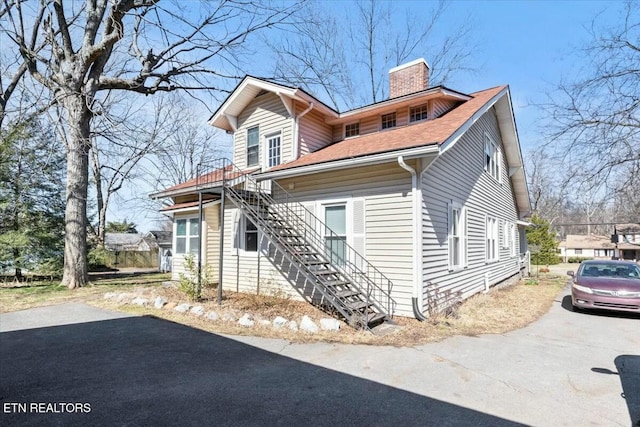 view of front of home featuring a shingled roof, stairs, and a chimney