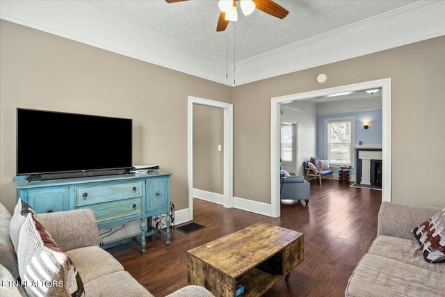 living area with ornamental molding, dark wood-style flooring, a fireplace with flush hearth, and a ceiling fan