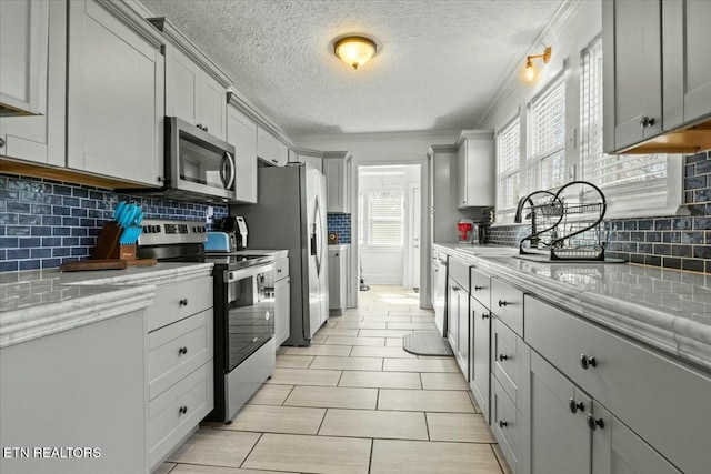 kitchen featuring a textured ceiling, light stone counters, appliances with stainless steel finishes, gray cabinets, and tasteful backsplash