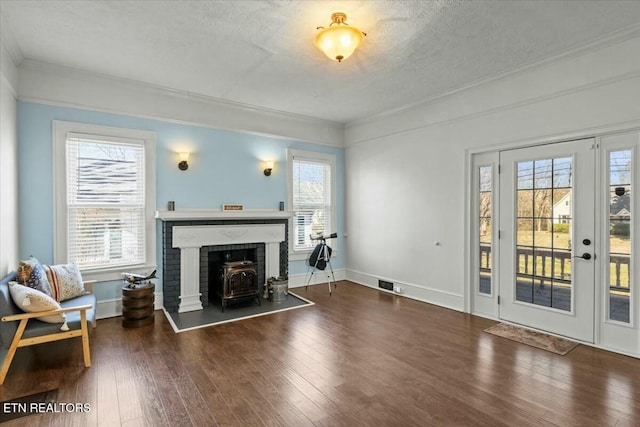 living area with crown molding, dark wood finished floors, a wood stove, a textured ceiling, and baseboards