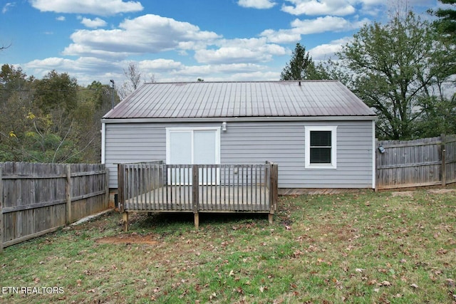 back of property with a wooden deck, a yard, a fenced backyard, and metal roof