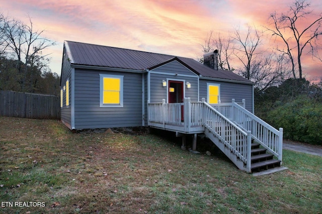 view of front of home featuring fence, a chimney, a front lawn, a deck, and metal roof