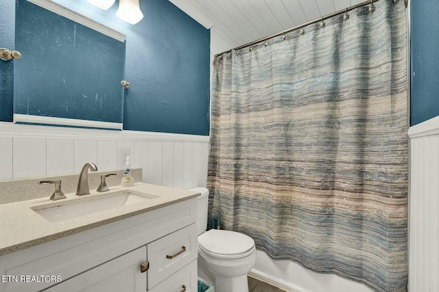 bathroom featuring vanity, shower / bath combination with curtain, toilet, and a wainscoted wall