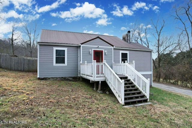 view of front facade with metal roof, a chimney, a front lawn, and fence