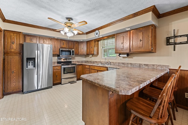 kitchen featuring appliances with stainless steel finishes, brown cabinets, a peninsula, crown molding, and a sink