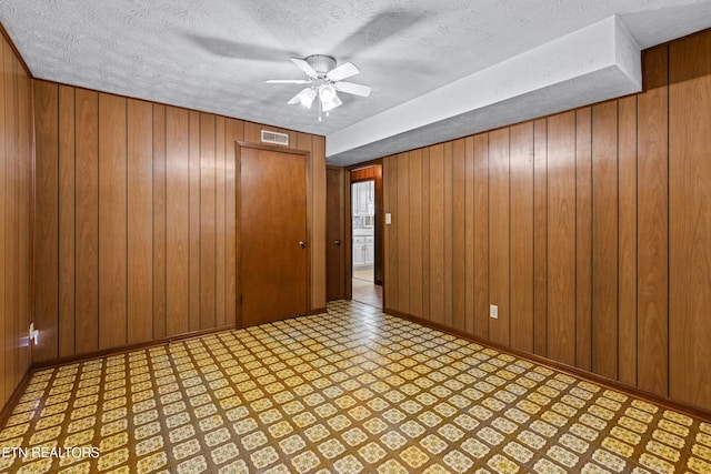 unfurnished room with light floors, visible vents, a ceiling fan, wooden walls, and a textured ceiling