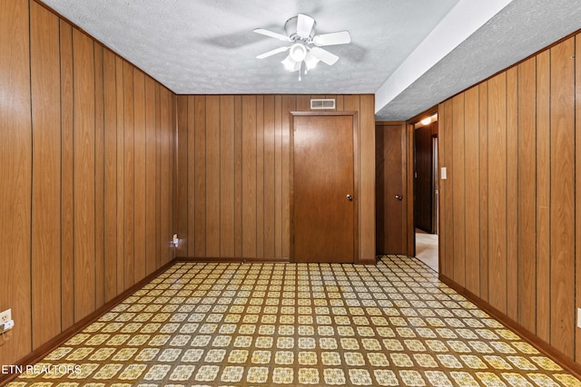 spare room with a ceiling fan, visible vents, wood walls, and baseboards