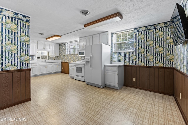 kitchen featuring white appliances, white cabinetry, light floors, and a wainscoted wall