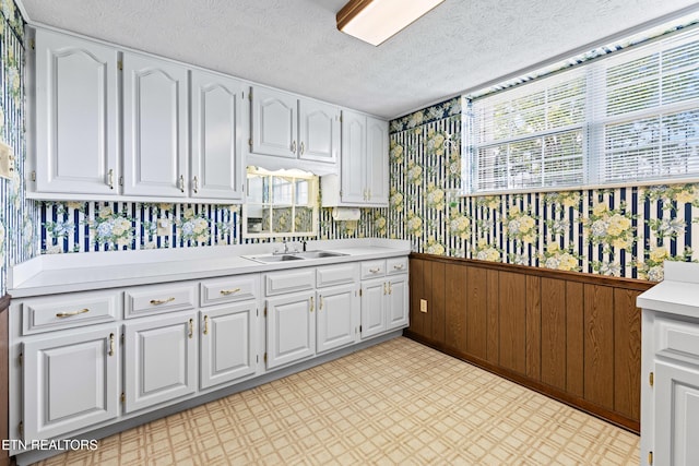 kitchen with wallpapered walls, white cabinetry, light countertops, and a wainscoted wall