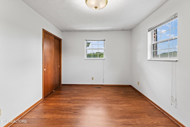 unfurnished bedroom featuring a closet, visible vents, dark wood-type flooring, a textured ceiling, and baseboards