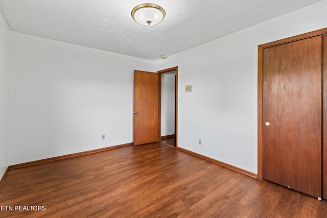 unfurnished bedroom with dark wood-style floors, a closet, a textured ceiling, and baseboards