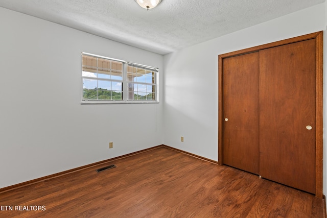 unfurnished bedroom featuring a textured ceiling, visible vents, baseboards, a closet, and dark wood-style floors