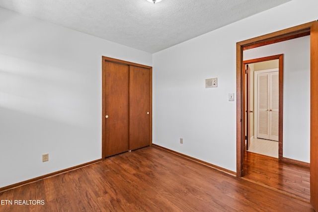 unfurnished bedroom featuring a textured ceiling, baseboards, and wood finished floors