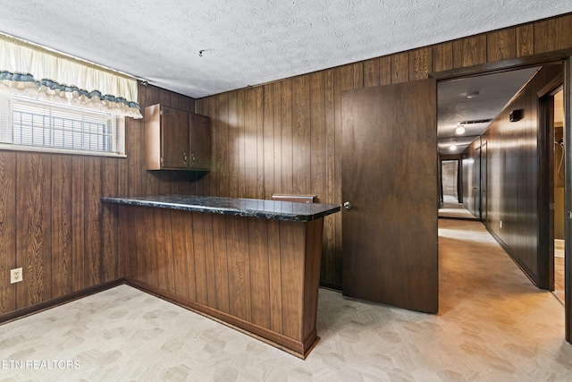 bar with a textured ceiling, wood walls, and baseboards