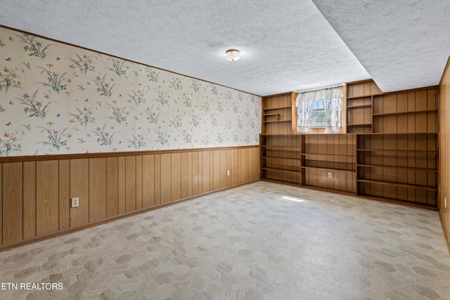 spare room with light carpet, wainscoting, a textured ceiling, wooden walls, and wallpapered walls