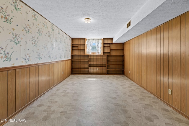 spare room featuring light colored carpet, wainscoting, wooden walls, a textured ceiling, and wallpapered walls