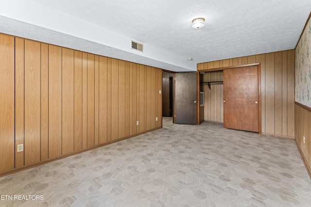 unfurnished bedroom featuring a textured ceiling, wood walls, visible vents, and baseboards