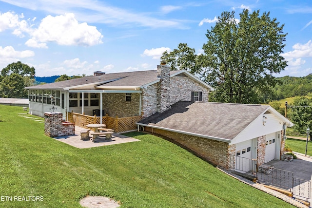 rear view of property with a yard, roof with shingles, a sunroom, and a patio