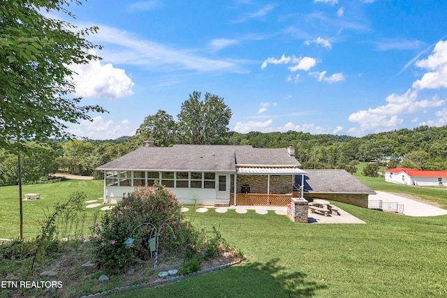 back of property featuring a sunroom, a patio, a chimney, and a lawn