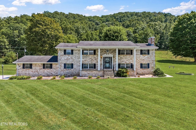 bi-level home featuring a forest view, a chimney, and a front lawn