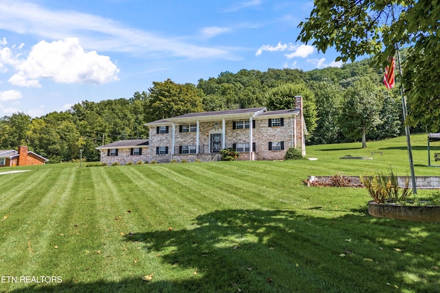 view of front of house featuring a forest view, stone siding, a chimney, and a front yard