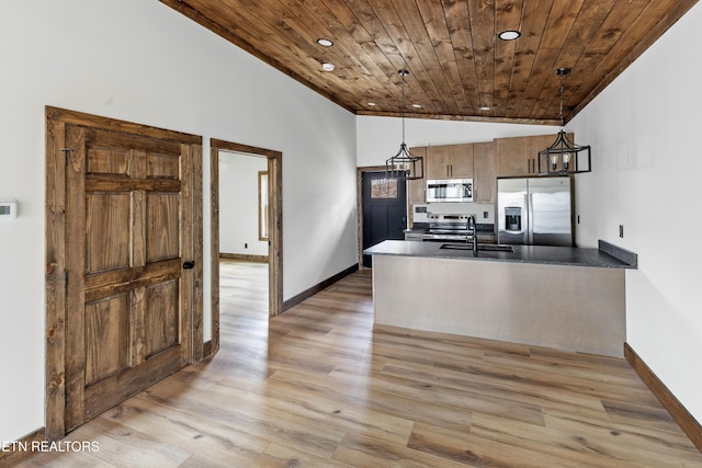 kitchen with a peninsula, vaulted ceiling, appliances with stainless steel finishes, dark countertops, and pendant lighting