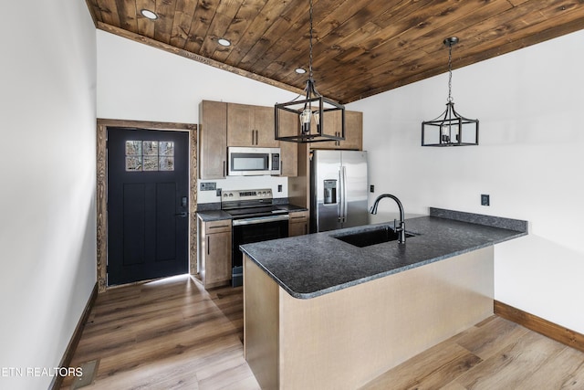 kitchen with hanging light fixtures, appliances with stainless steel finishes, dark countertops, and a sink