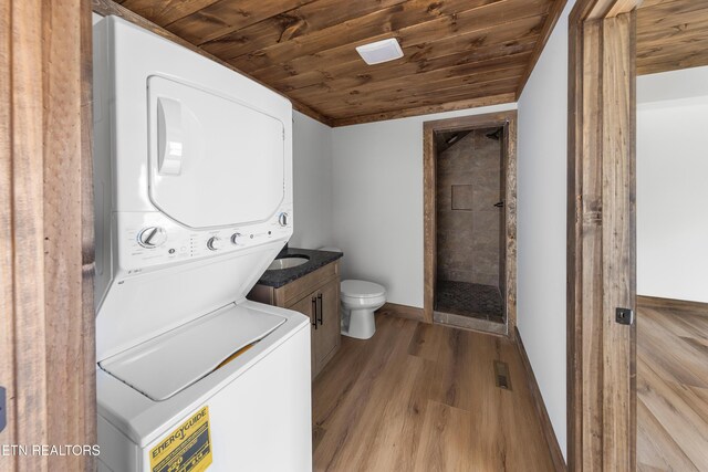 laundry area featuring laundry area, stacked washer and dryer, wood ceiling, baseboards, and light wood-type flooring