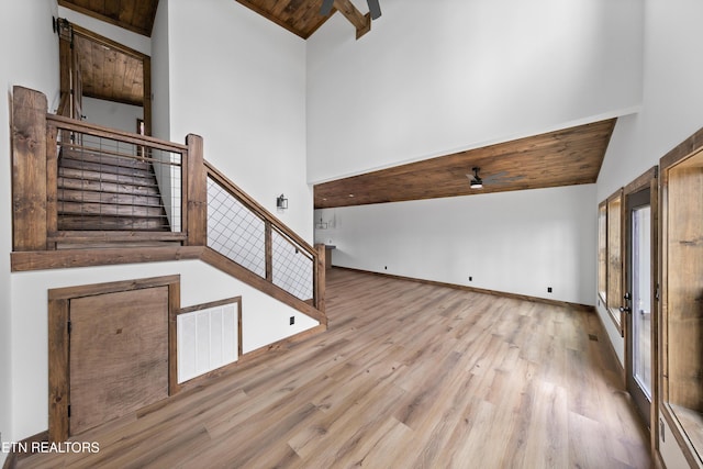 unfurnished living room featuring stairway, light wood-type flooring, a towering ceiling, and visible vents