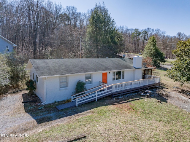 view of front of property with a deck, brick siding, a forest view, a front lawn, and a chimney