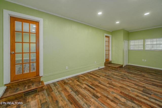 empty room with dark wood-style flooring, visible vents, crown molding, and baseboards