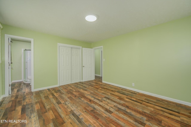 unfurnished bedroom featuring a closet, dark wood-style flooring, ensuite bath, and baseboards