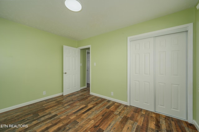 unfurnished bedroom with a closet, dark wood-style flooring, and baseboards