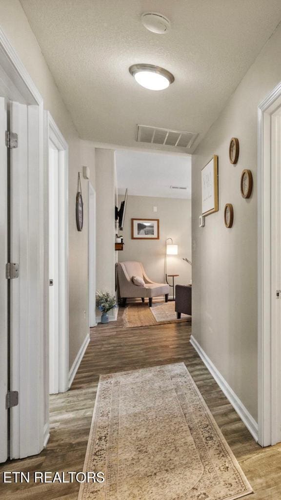 hallway featuring a textured ceiling, wood finished floors, visible vents, and baseboards