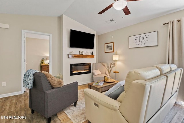 living room featuring lofted ceiling, ceiling fan, wood finished floors, visible vents, and a glass covered fireplace