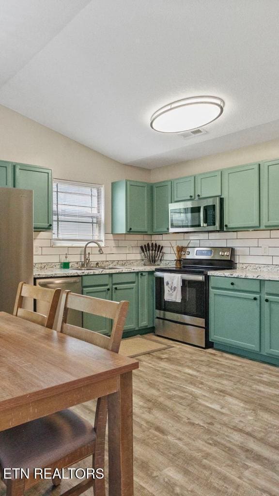 kitchen featuring light wood-style floors, tasteful backsplash, appliances with stainless steel finishes, and green cabinetry